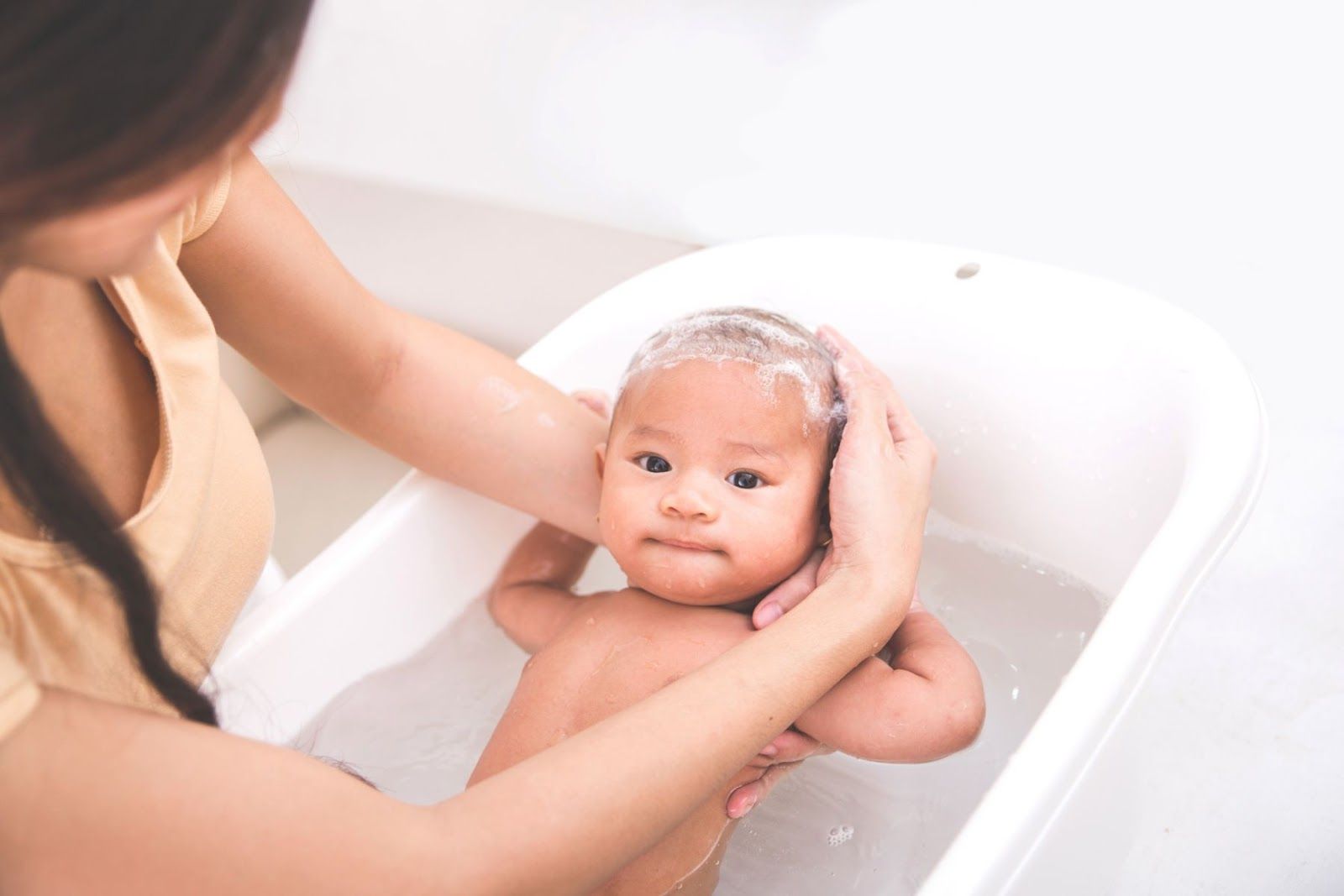 Vệ sinh nhẹ nhàng bằng nước ấm cho trẻ khi bị tay chân miệng (Nguồn: Canva)